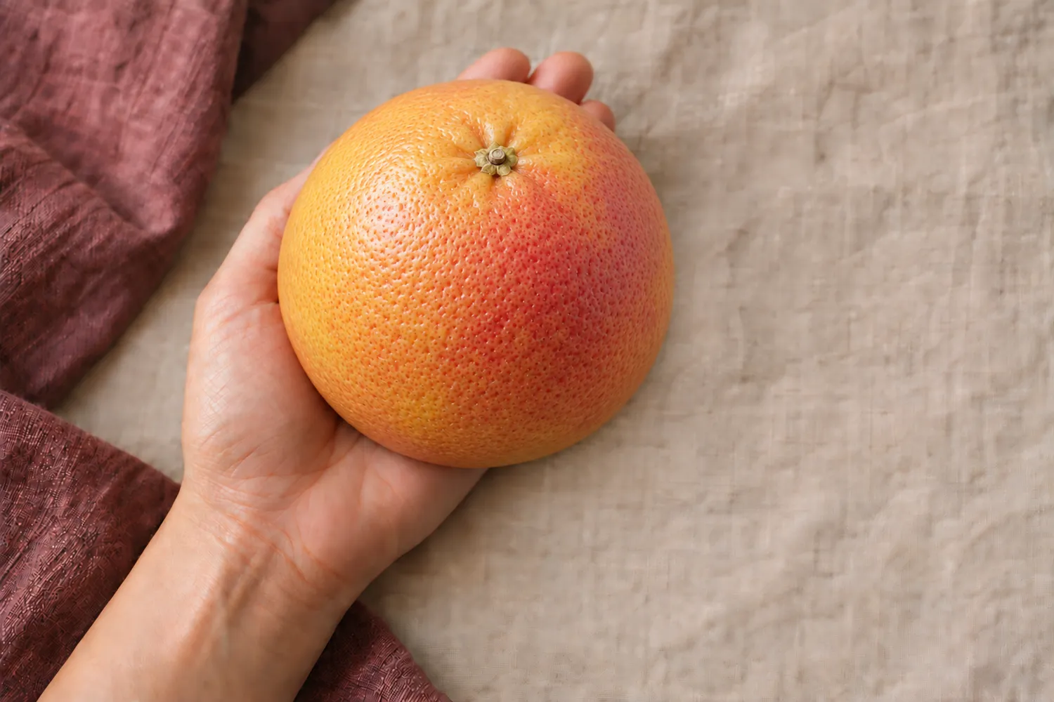 Een enkele grapefruit ligt in een open handpalm op beige linnen